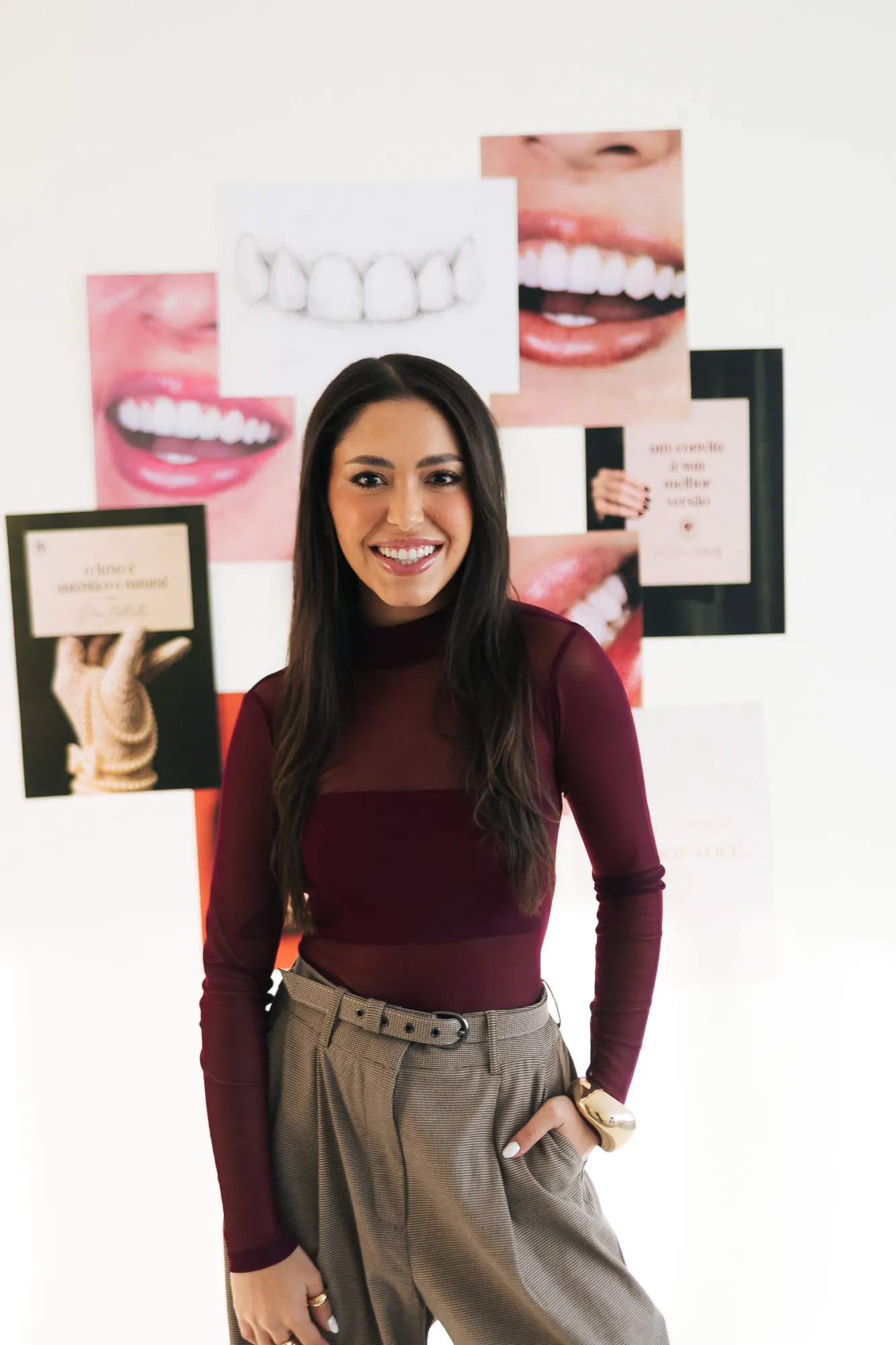 Dra. Nathielly Leite sorrindo diante de um mural de sorrisos no consultório